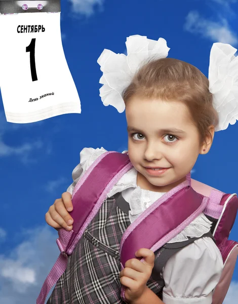 Russia - September 1: first grader in her school uniform with knapsack on the background of blue sky with the calendar sheet. Collage.