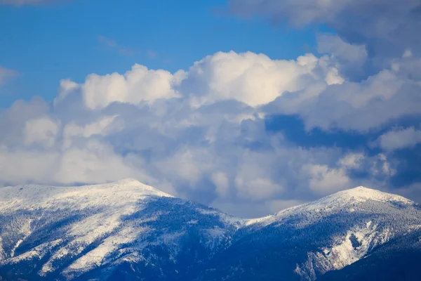 Snowy mountain range with blue sky and clouds.