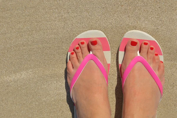 Womans feet with flip flops on the sand