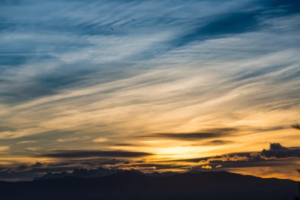 Sunlight behind dark mountain silhouettes, with blue and orange colored and clouds