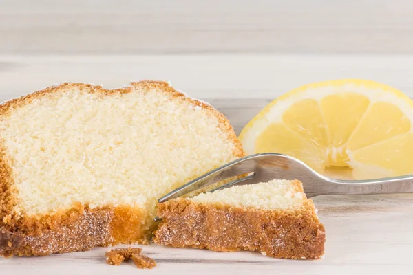 Closeup of a piece of lemon cake with a fork and lemon fruit