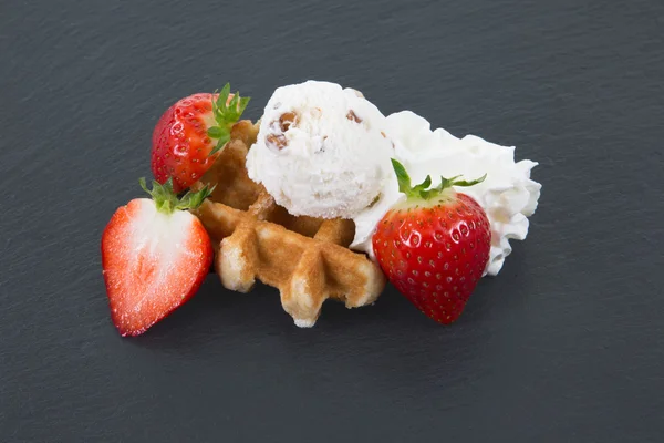Round waffle decorated with ice, strawberry and cream laying on dark slate