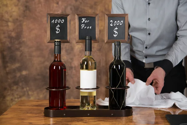 Waiter is decorating three wine bottles with a price board for s