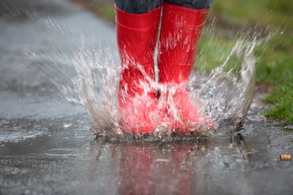 Rubber boots are jumping into a big puddle with splash