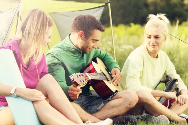 Friends camping in forest and playing guitar