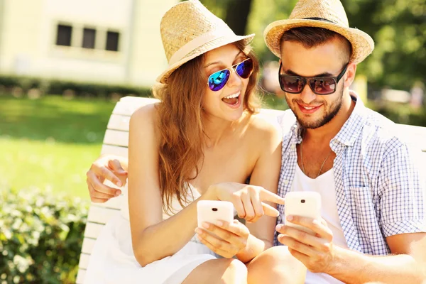 Happy couple sitting on a bench with smartphones