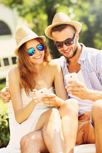 Joyful couple sitting on a bench with smartphones