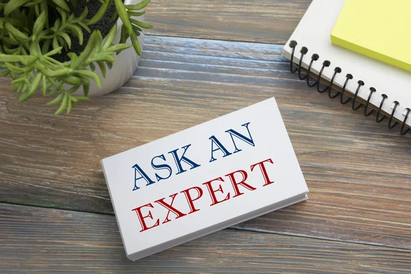 Ask an expert. Business card with message, notepad and flower. Office supplies on desk table top view.