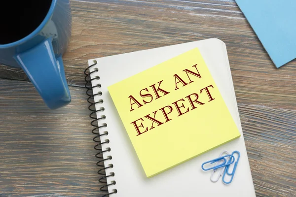 Ask an expert. Notepad with message and coffee cup. Office supplies on desk table top view.