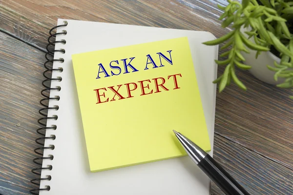 Ask an expert. Notepad with message, pen, reminder and flower. Office supplies on desk table top view.