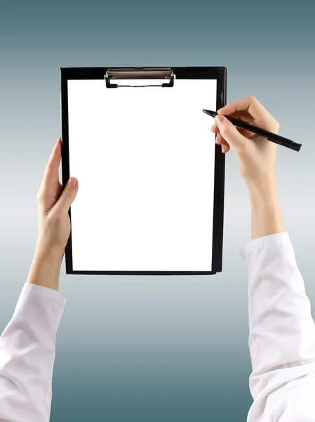 A female hand holding a pen and clipboard with blank paper (document, report) on blurred background. Top view.