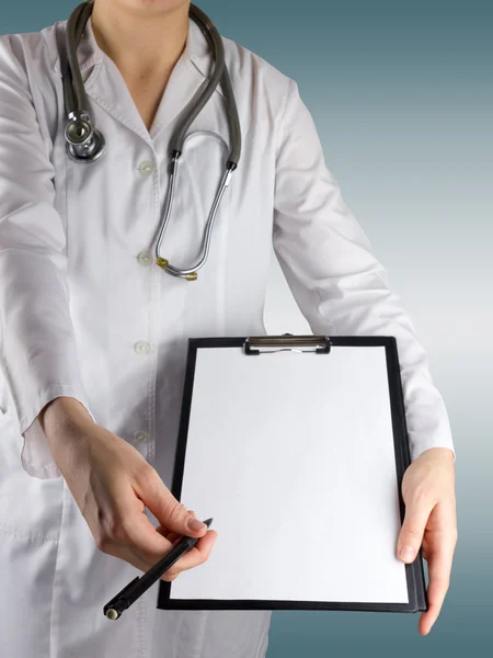 Female Doctor\'s hand holding a pen and clipboard with blank paper (document, report) and stethoscope on blurred background. Concept of Healthcare And Medicine. Copy space