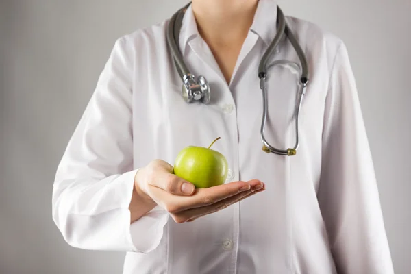 Female doctor\'s hand holding green apple. Close up shot on grey