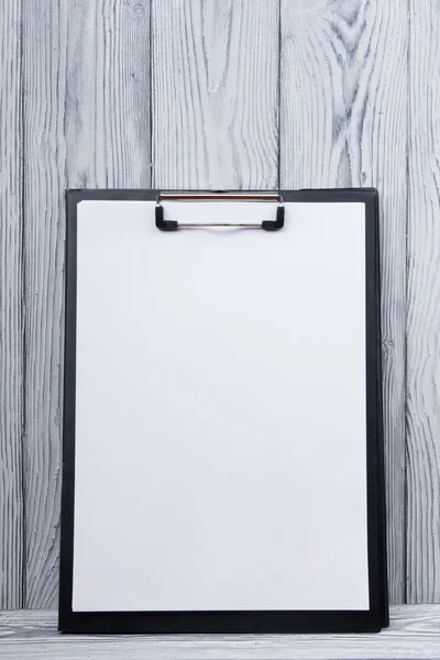 Clipboard with blank sheet of paper on wood background. Copy space