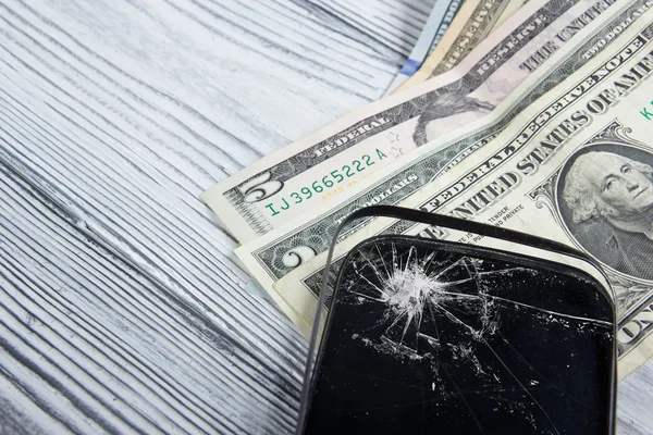 Modern broken mobile phone and money on white wooden background. Copy space. Top view