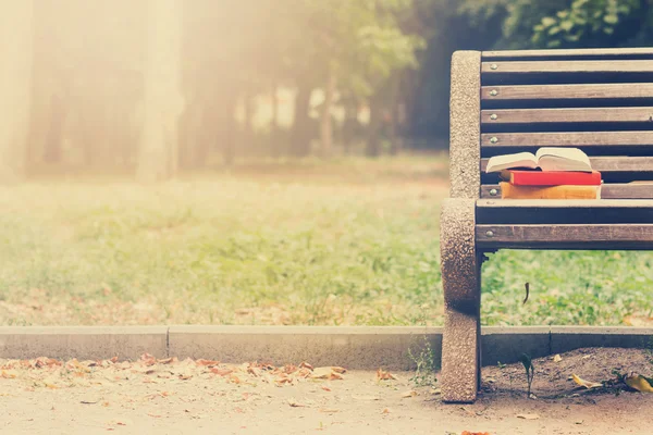 Stack of hardback books and Open book lying on bench at sunset park against blurred nature backdrop. Copy space, back to school. Education background. Toned image