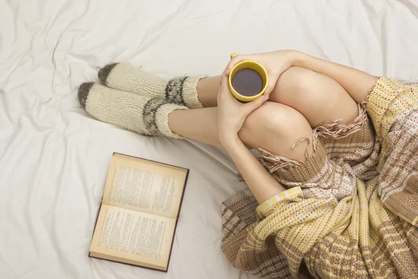 Woman on the bed with old book and cup of coffee in hands, top view point. Copy space for text. Soft photo