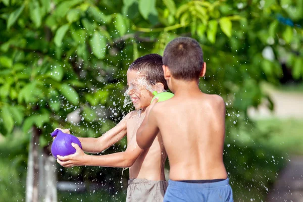 Children outside on a summer day, sprayed with balloons filled w
