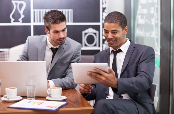 Two young businessman working on a digital tablet in a cafe