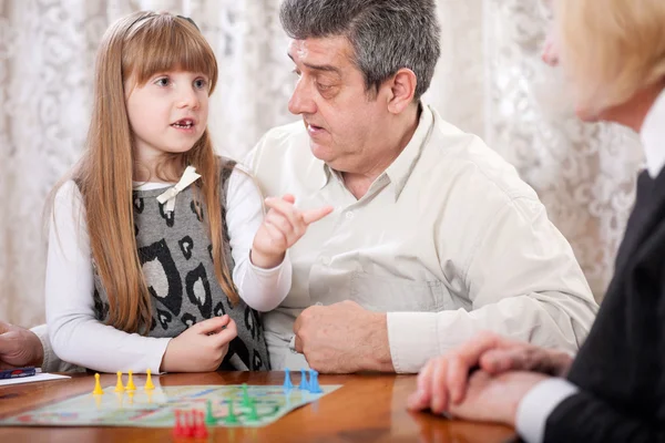 Smiling grandfather, grandmother and granddaughter playing board