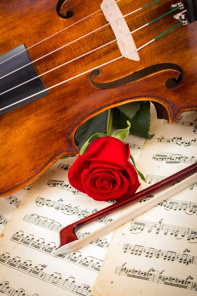 Violin, red rose and bow on score