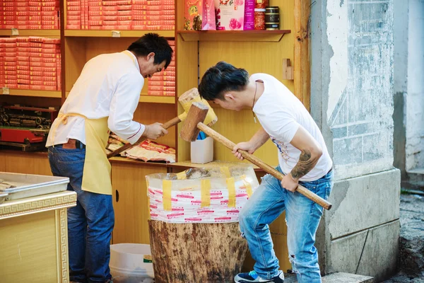 Chinese men with wooden mallets are crushing nuts, Lijiang