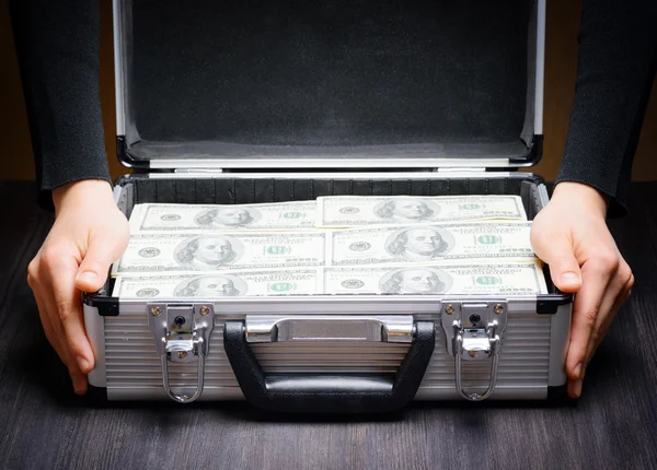Business man opens an aluminum briefcase full of stacks of hundr
