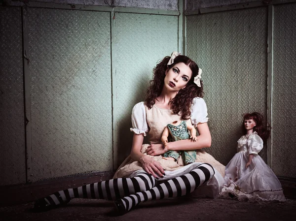 Strange sad girl with dolls sitting in forsaken place