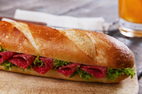Baguette sandwich with salami and herbs on a wooden surface