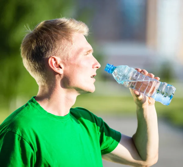 Tired man drinking water from a plastic bottle after fitness