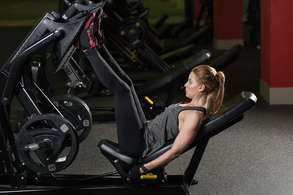 Sportive woman using weights press machine for legs. Gym.