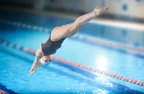 Female swimmer jumping into swimming pool.