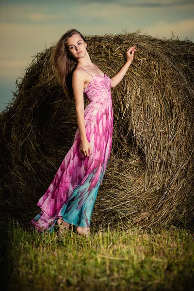 Woman standing in evening field over haystack.