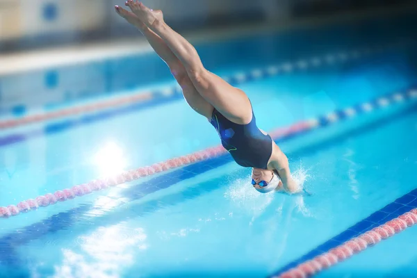 Female swimmer, that jumping into indoor swimming pool.