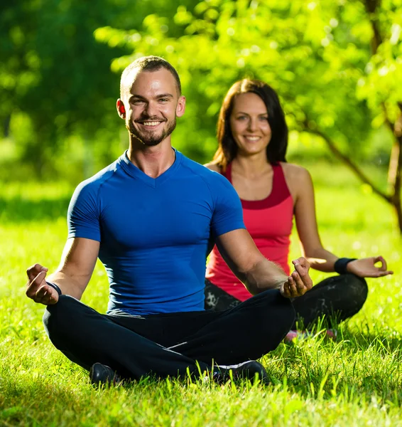 Young man and woman doing yoga in the sunny summer park