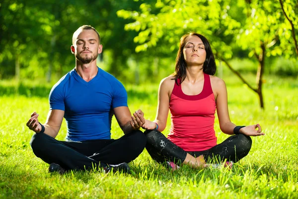 Young man and woman doing yoga in the sunny summer park