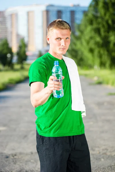 Tired man with white towel drinking water from a plastic bottle