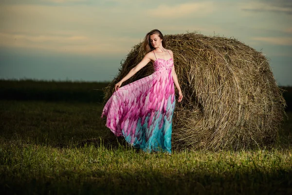 Young woman standing in evening field over haystack. Fashion sty