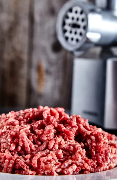 Raw ground beef on a white plate with meat grinder