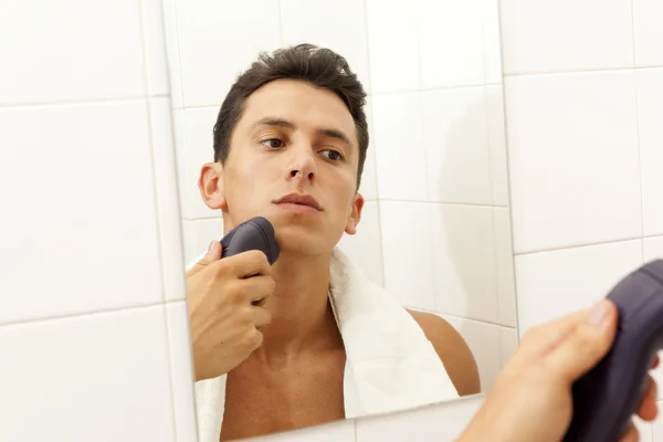 Young man shaving with electric shaver at the bathroom