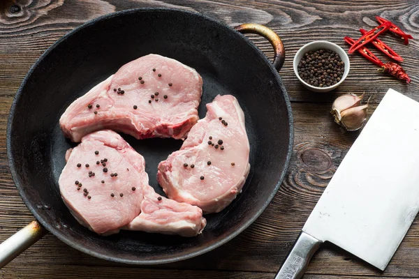 Raw Pork Loin Steaks in a pan on wooden table