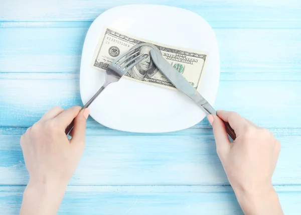 Empty plate cutlery in hands concept we eat money business lunch table wood background gentle blue tone