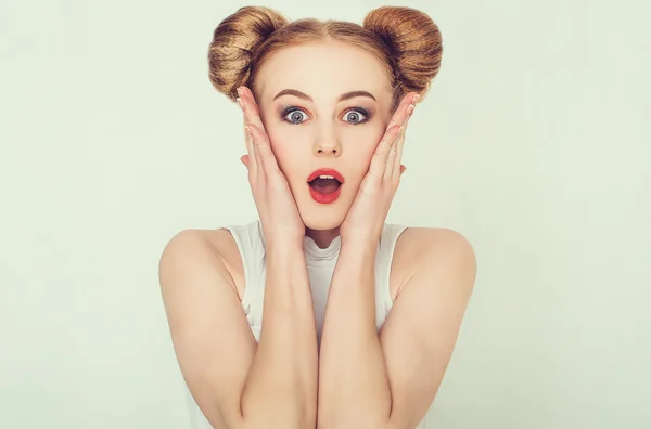 Close-up portrait of surprised beautiful girl with funny hairstyle holding her head in amazement and open-mouthed.