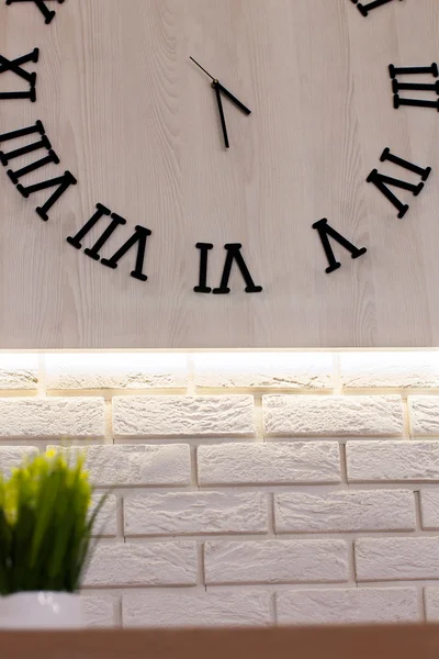 Wooden clock with Roman numerals on a white brick wall