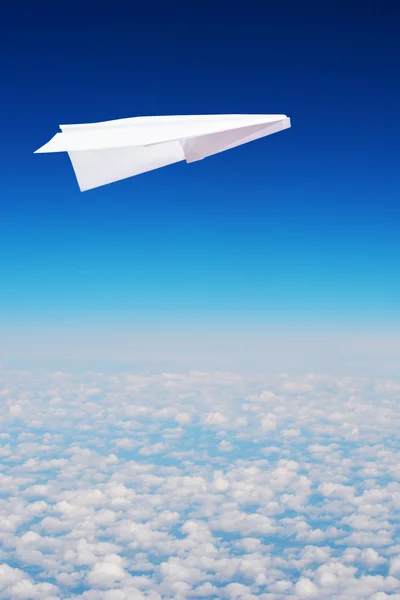 Toy paper plane flies high in the sky over clouds