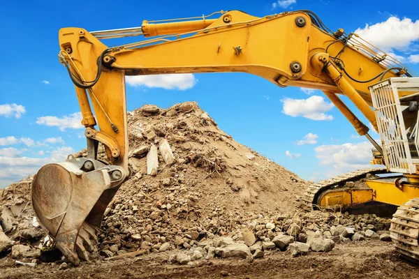 Excavator and heap of dirt in front of blue sky