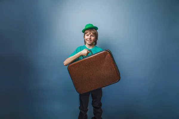 European-looking boy of ten years in a hat holding a suitcase in hand, itinerary on a blue background