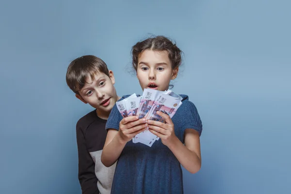 Girl holding money bills in the hands of the boy opened his mout