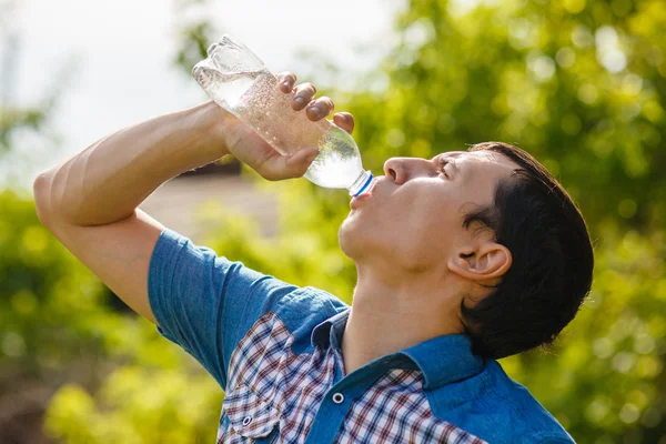 Man drinks water from a plastic bottle on the street in the summ