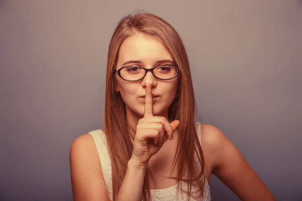 European-looking girl of twenty years with glasses, finger to li